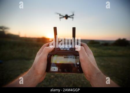 Blickpunkt des Mannes, der die Fernbedienung mit den Händen hält und Luftfoto-Videos mitnimmt. Quadcopter flieht im Hintergrund. POV - Drohne Stockfoto