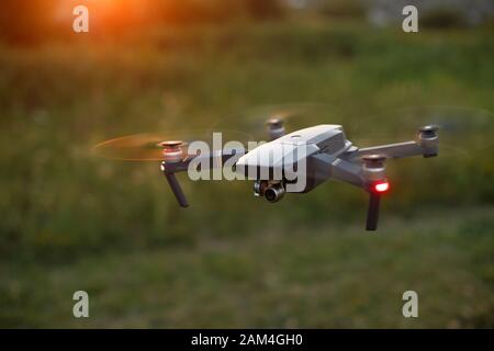 Kleiner kompakter Quadcopter fliegt bei Sonnenuntergang in der Luft. Drohne schwebt und bleibt stabil. Stockfoto