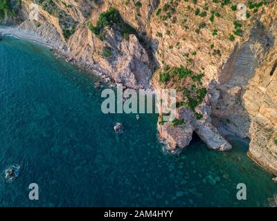 Luftaufnahme von einem steilen Felsen und ein Motorboot. Zerklüftete Küste an der Adria. Klippen mit Blick auf den transparenten Meer. Budva, Montenegro Stockfoto