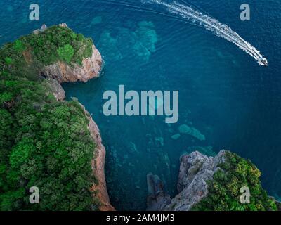 Luftaufnahme von einem steilen Felsen und ein Motorboot. Zerklüftete Küste an der Adria. Klippen mit Blick auf den transparenten Meer. Budva, Montenegro Stockfoto