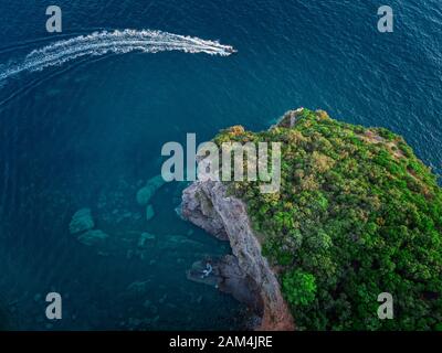 Luftaufnahme von einem steilen Felsen und ein Motorboot. Zerklüftete Küste an der Adria. Klippen mit Blick auf den transparenten Meer. Budva, Montenegro Stockfoto