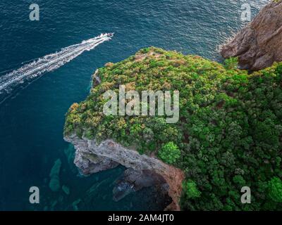 Luftaufnahme von einem steilen Felsen und ein Motorboot. Zerklüftete Küste an der Adria. Klippen mit Blick auf den transparenten Meer. Budva, Montenegro Stockfoto