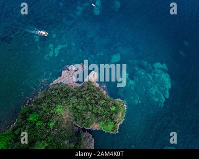 Luftaufnahme von einem steilen Felsen und ein Motorboot. Zerklüftete Küste an der Adria. Klippen mit Blick auf den transparenten Meer. Budva, Montenegro Stockfoto