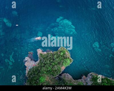 Luftaufnahme von einem steilen Felsen und ein Motorboot. Zerklüftete Küste an der Adria. Klippen mit Blick auf den transparenten Meer. Budva, Montenegro Stockfoto