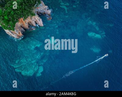 Luftaufnahme von einem steilen Felsen und ein Motorboot. Zerklüftete Küste an der Adria. Klippen mit Blick auf den transparenten Meer. Budva, Montenegro Stockfoto
