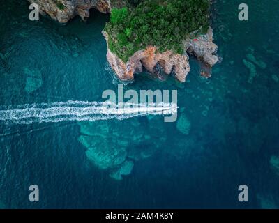 Luftaufnahme von einem steilen Felsen und ein Motorboot. Zerklüftete Küste an der Adria. Klippen mit Blick auf den transparenten Meer. Budva, Montenegro Stockfoto