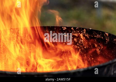 Nahaufnahme von roten, gelben und orangefarbenen Flammen in einem geschwärzten alten Metallbehälter Stockfoto