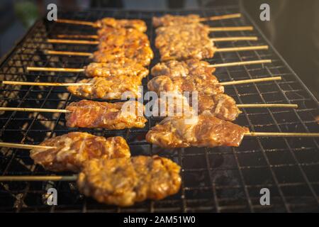 Heiße und frische, thailändisch gegrillte Schweinefleischspieße, beliebte Straßengerichte in Thailand, auf einem Holzkohlenofen. Stockfoto