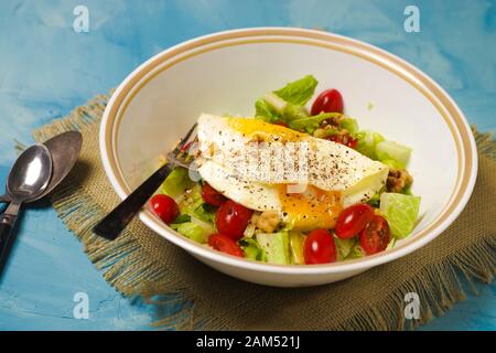 Grüner Salat mit Ei-Omelett in Untertasse mit Metallgabel und Löffel auf blauem Grund Stockfoto