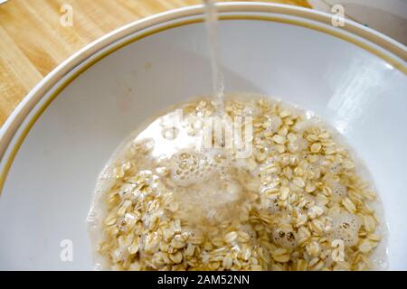 Frühstück - Haferflocken in Weiß Schüssel, Wasser gegossen auf trockenem, Hafer vor dem Kochen gerollt Stockfoto