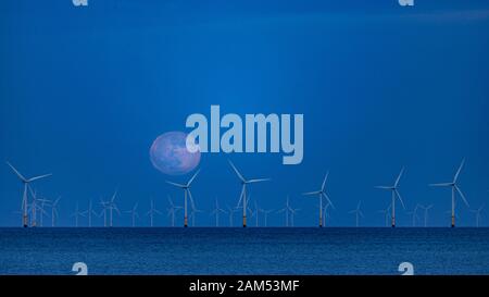 Vollmond steigt in der Dämmerung über Offshore-Windturbinen Stockfoto