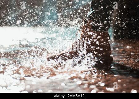 Flusswasser spritzt auf einem orangefarbenen Mannstiefel. Eingefrorener Moment, Action Shot. Blauer Wasserfall in der Ferne. Stockfoto