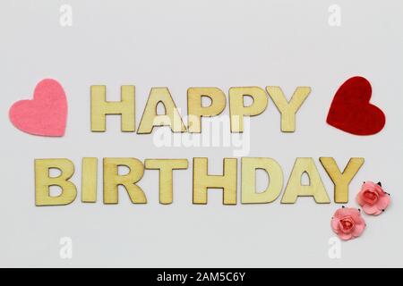 Alles gute zum Geburtstag mit Holzbuchstaben auf weißer Oberfläche, Herzen und pinkfarbenen Papierrosen Stockfoto