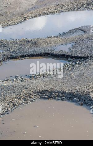 Große Schlaglöcher mit stehenden Wasserpfützen auf einem Parkplatz am Meer in Cornwall. Metapher holprig, unebene Oberfläche, in schlechtem Zustand, reparaturbedürftig. Stockfoto