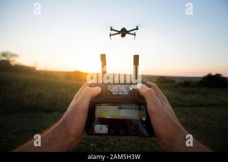 Blickpunkt des Mannes, der die Fernbedienung mit den Händen hält und Luftfoto-Videos mitnimmt. Quadcopter flieht im Hintergrund. POV - Drohne Stockfoto
