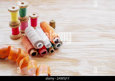 Auf einem Holztisch liegen Nahtstellen verschiedener farbiger Spulen von Nähfaden. Kopierbereich. Stockfoto