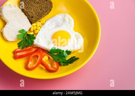 Herzförmiges frittiertes Ei und Brot in gelber Platte auf rotem Grund. Valentines Tageskonzept Stockfoto