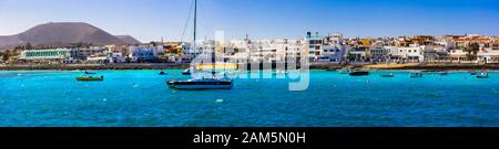 Wunderschönes Dorf in Corralejo, Blick auf türkisfarbenes Meer, Berge und traditionelle Fischerboote, Fuerteventura, Spanien. Stockfoto