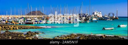 Wunderschönes Dorf in Corralejo, Blick auf traditionelle Fischerboote, türkisfarbenes Meer und Berge, Insel Fuerteventura, Spanien. Stockfoto