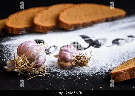 Inschriftenbäckerei auf Weißweizenmehl verstreut Geschnittenes Roggenbrot mit Knoblauch auf dunklem Grund Stockfoto