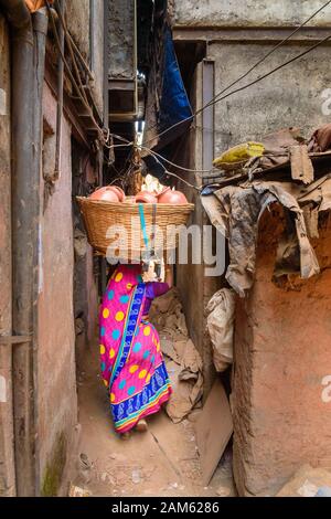 Indianerin trägt Korb mit Tontöpfen auf dem Kopf auf der Straße in Dharavi Slum in Mumbai. Indien Stockfoto