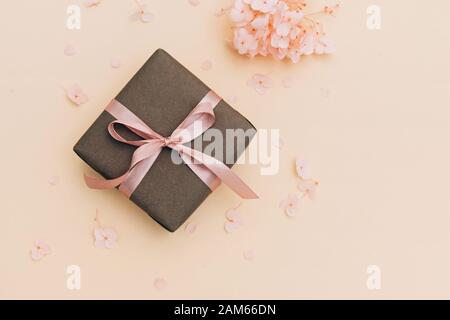 Geschenkschachtel in Handarbeit mit rosafarbenem Band auf hellorangefarbenem Hintergrund mit Hydrangea-Blumen verpackt. Stockfoto