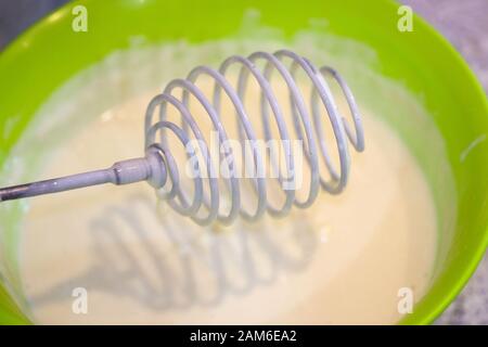 Metall-Schneebesen mit Schlagblech in Minsk. Teig für Pfannkuchen mit einem Handscheitel herstellen. Mit einem Holzgriff in Form einer Feder schlagen. Stockfoto