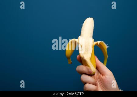 Geschälte gelbe Bananenfrucht nahe blauem Hintergrund in der Hand, gesundes Konzept Stockfoto