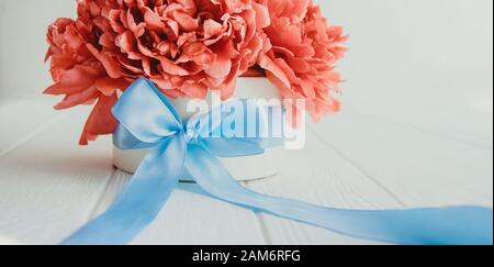 Beschnitten schöner roter, pfriemlicher Blumenstrauß in runder Schachtel mit blauer Sattin-Schleife auf weißem Holzhintergrund. Geschenk, Gruß, Komplimentsidee. Weit Stockfoto