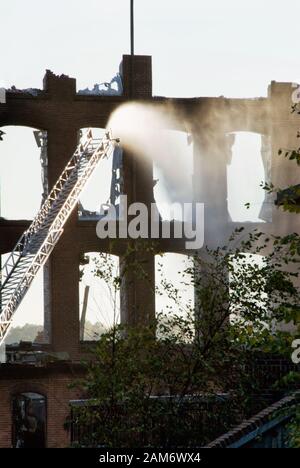 Feuerwehrleute, die in einem Industriegebäude einen Brand ausbrechen, indem sie einen Feuerwehrwagen verwenden, der Wasser aus der Leiter herausschießt, die am Feuerwehrmotor befestigt ist. Stockfoto