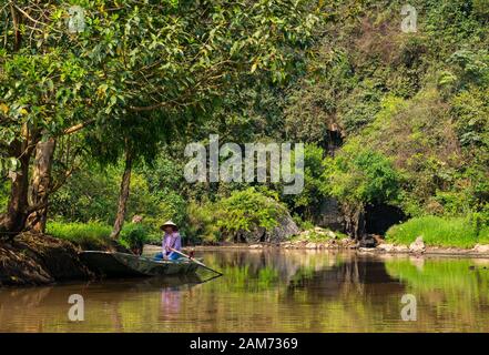 Asiatische Frau mit konischem Hut in Sampan am Fluss mit Eingang der Höhle, Tam Coc Höhlensystem, Ninh Binh, Vietnam, Asien Stockfoto