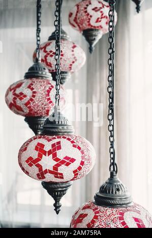 Nahaufnahme eines Kristallleuchters, selektiver Fokus und gewollter Unschärfe. Türkische hängende bunte Glasleuchte aus rot-weiß gestanzten Pflafond Stockfoto