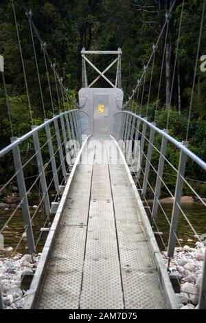 Gehen Sie auf dem Old Ghost Road Trail, Lyell nach Seddonville, Neuseeland. Possum Proof Brückentür auf einer Fußgängerbrücke über den südlichen Zweig des Flusses Mokinhinui Stockfoto