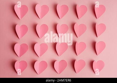 Pinke Papierherzen auf rosa Hintergrund. Papierherzen in Reihen auf rosa Hintergrund angeordnet. Flach liegend Stockfoto