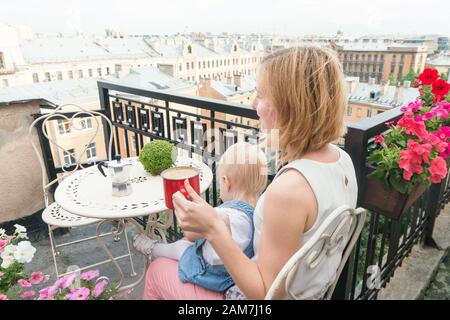 Mutter mit Kaffeepause, während sie mit einem Baby auf dem Balkon sitzt Stockfoto