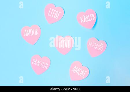 Einige herzförmige pinke Haftnotizen mit dem Wort Liebe, die in verschiedenen Sprachen geschrieben wurden, wie Englisch, Spanisch, Italienisch, Französisch, Niederländisch auf blauem Hintergrund. Valentinstag, Liebeskonzept. Stockfoto