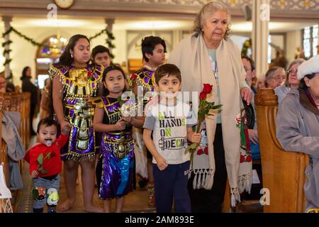 Detroit, Michigan, USA. Januar 2020. Eine "heilige Stunde" in Der Katholischen Dreifaltigkeitskirche unterstützte Flüchtlinge, die vor Gewalt in ihren Heimatländern fliehen. Mary Turner, rechts, begleitet Kinder, die während eines Kindergebets Rosen zum Altar bringen. Die Veranstaltung wurde von Fremden nicht Mehr während der U.S. Catholic Bishops' National Migration Week organisiert. Kredit: Jim West/Alamy Live News Stockfoto