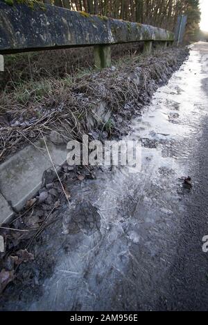 Gefrorenen Pfütze auf der Seite der ein Feldweg in der Landschaft in der Nähe des Waldes Stockfoto