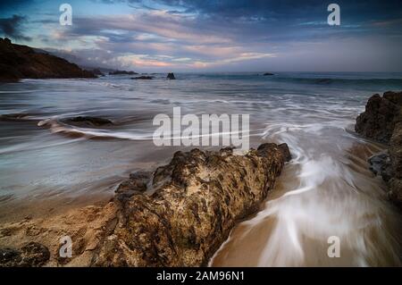 Dynamische Wellen in den Strand fegen an einem bewölkten Tag Stockfoto