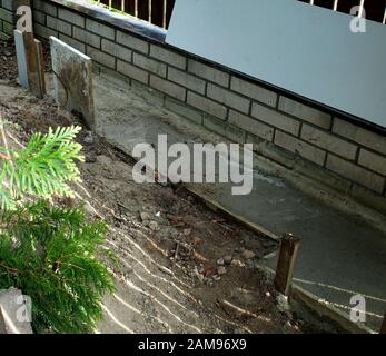 Vor kurzem gegossen, Beton Stiftung unter dem Gartenzaun Stockfoto