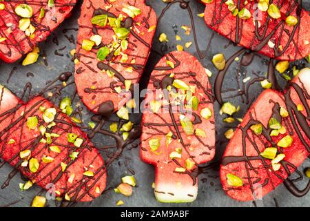 Slices Wassermelone in Eis- oder poppiger Form mit Schokolade und Pistaziennüssen Dekoration, Draufsicht Stockfoto