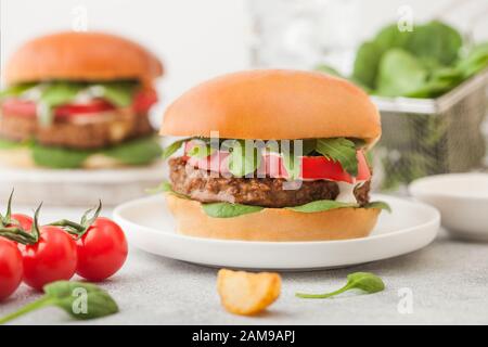 Gesunde vegetarische, fleischfreie Burger auf runder Keramikplatte mit Gemüse und Spinat auf hellem Hintergrund. Stockfoto