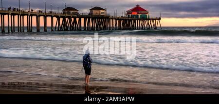 Malerische Landschaft des Huntington Beach Pier bei Sonnenuntergang. Das menschliche Element, die natürlichen Elemente und die menschlichen Elemente kommen zu goldener Stunde zusammen. Stockfoto