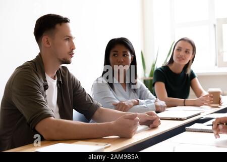 Multiethnische Mitarbeiter hören Teamleiter zuversichtlich bei Gruppentreffen Stockfoto