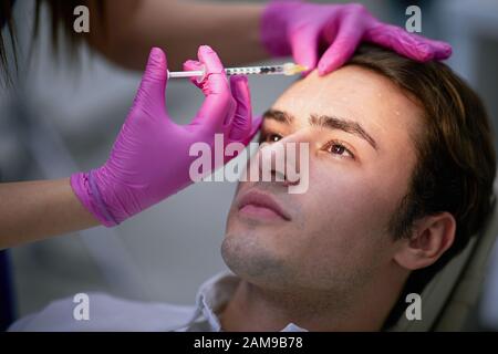 Junger Mann, der seine Stirnfalten mit eingesteckter Substanz des Muskelbewegungshemmers reduziert hat Stockfoto