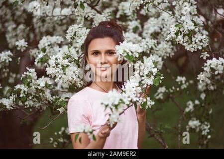 Mädchen steht im blühenden Apfelbaum im Frühlingspark Stockfoto