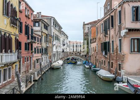 Venedig, ITALIEN - 31. Oktober 2019: Stadtbild mit vermoorten Booten im Kanal und Lastkahn, die unter niedriger Brücke segeln, am 31. oktober 2019 in hell bewölktem Tal gedreht Stockfoto