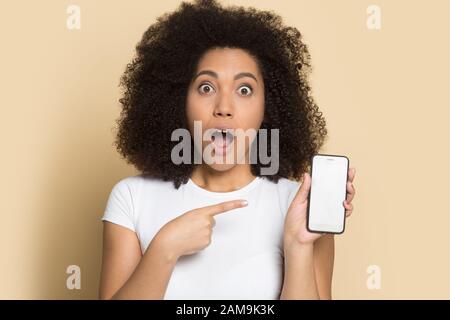 Überraschte das afroamerikanische Mädchen, das auf einen verspotteten Telefonbildschirm zeigt. Stockfoto