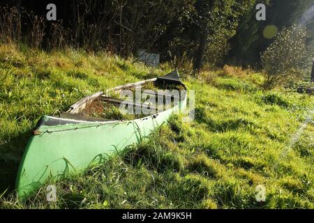 Das alte Kanu liegt auf der Wiese in Flussnähe und ist verlassen, von Gras überwuchert und nutzlos. Stockfoto
