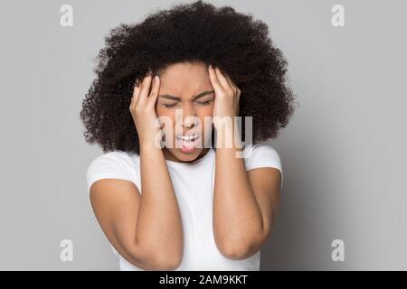 Unglückliche junge afroamerikanische Frau, die unter starkem Kopfschmerzen leidet. Stockfoto